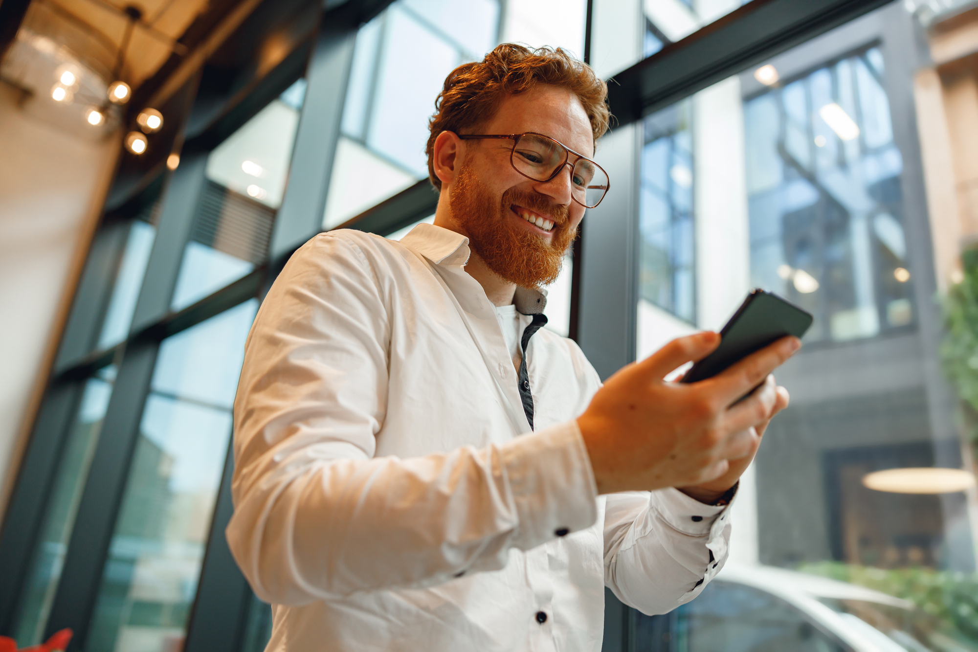 Bearded male freelancer holding phone while standing in office during break time