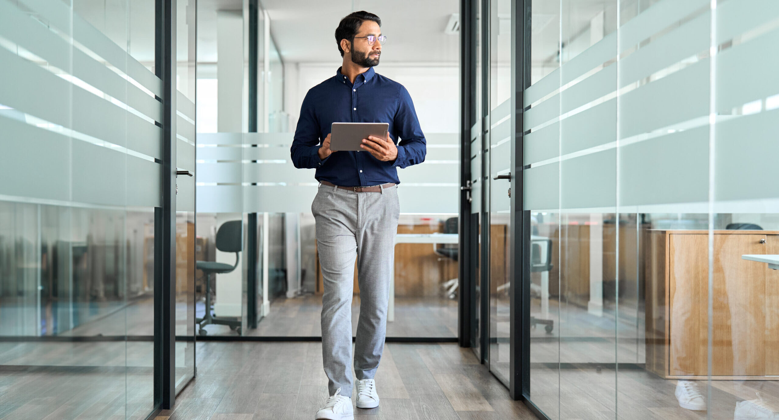 Busy professional businessman walking in office hallway holding digital tablet thinking of work plan. Authentic photo.