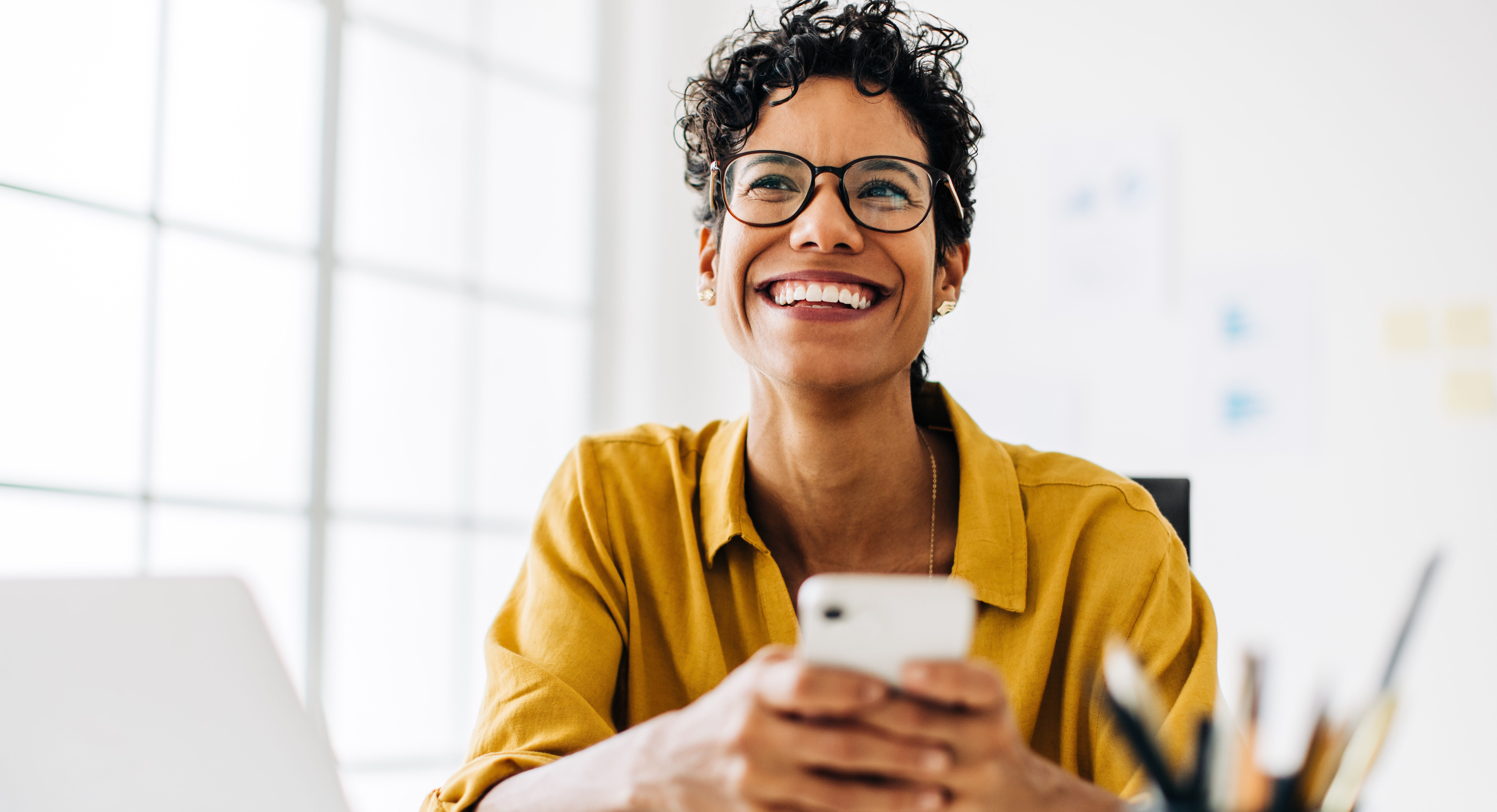 Professional black woman smiling and using a mobile phone. Business woman checking her messages while working from her desk.